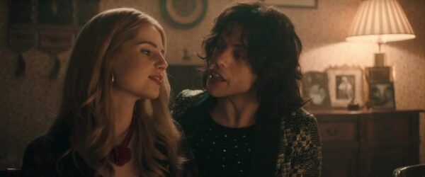 Freddie Mercury (Rami Malek) e Mary Austin (Lucy Boynton) no filme "Bohemian Rhapsody" (2018). Fotografia mostra cena do filme "Bohemian Rhapsody". A esqueda, vemos Mary Austin, uma mulher branca e loira de olhos claros, à esquerda, Freddie Mercury, um homem com cabelos pretos de tamanho médio 