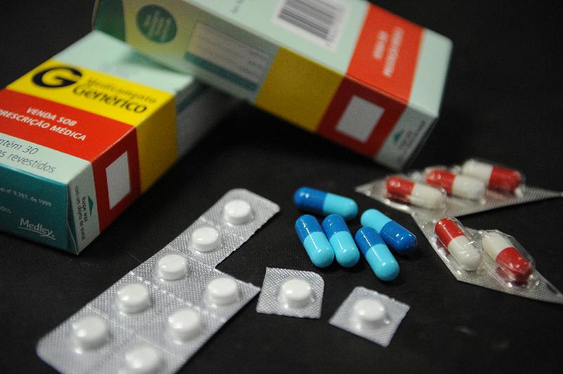 Remédios colocados sobre uma mesa. Há três tipos diferentes de comprimidos ou pílulas. Há ainda duas caixas de medicamentos genéricos não identificáveis.