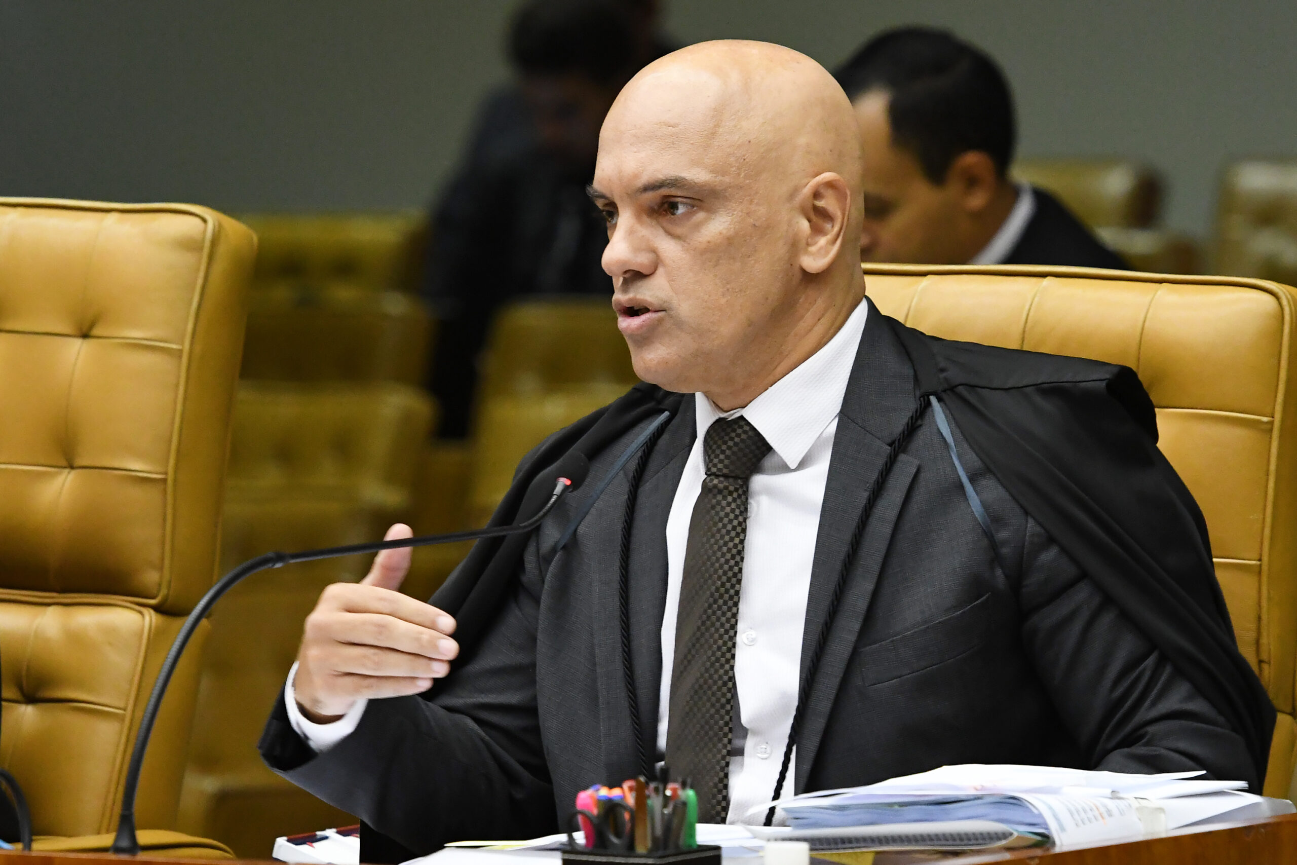 Alexandre de Moraes de terno, gravata e túnica fala em frente a um microfone