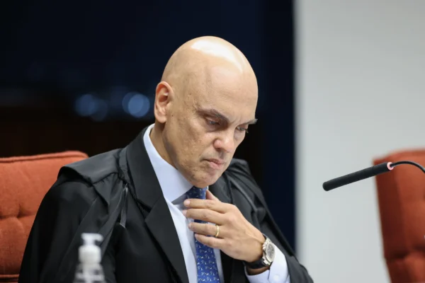O ministro do STF, Alexandre de Moraes, em sessão na corte. Ele é um homem careca, está sentado, usa terno e arruma a gravata com uma das mãos