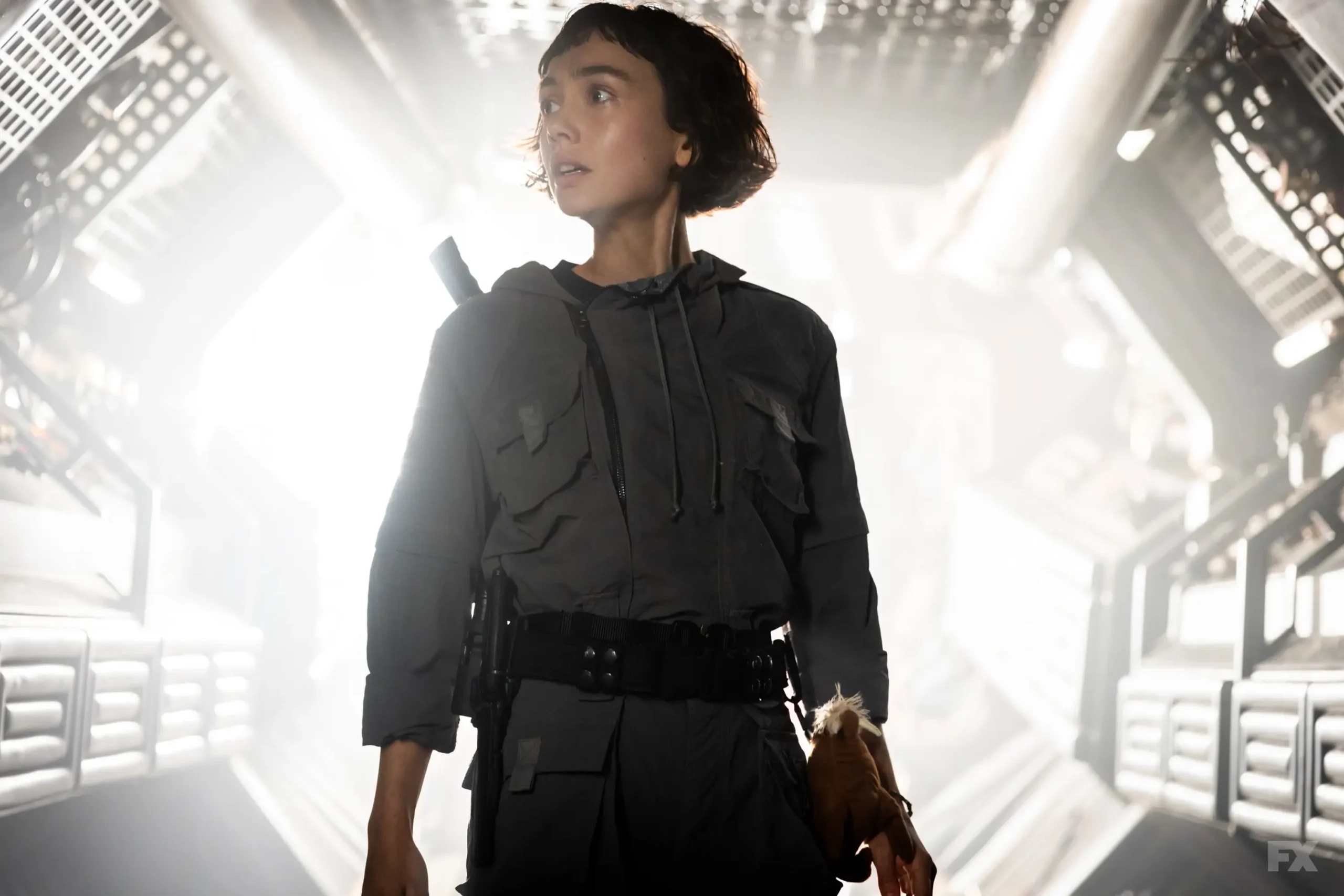 Cena de "Alien: Earth" (2025). Uma mulher está posicionada a frente uma portal com luz