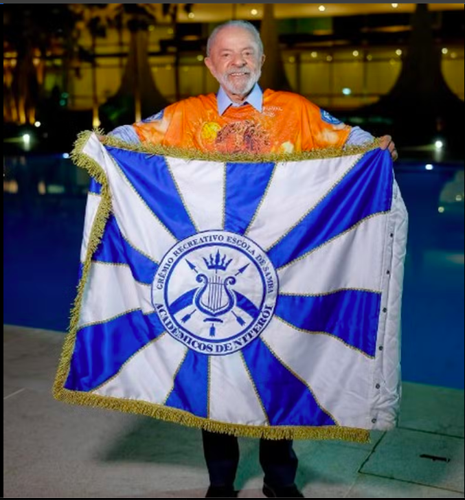 Presidente Lula segunra bandeira azul, branca e dourada da escola de samba Acadêmicos de Niterói