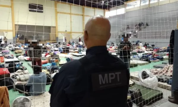 Trabalhadores resgatados de trabalho análogo à escravidão no RS. As pessoas estão em um ginásio e um agente do MPT as observa