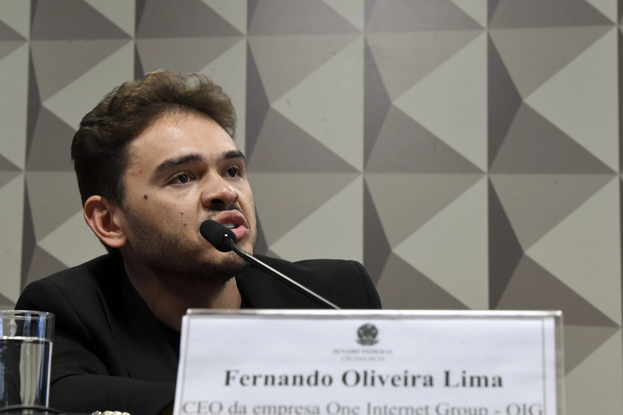 Fernandin OIG, em depoimento na CPI das Bets, em novembro de 2024. Um homem fala em um microfone. Ele está atrás de uma placa branca