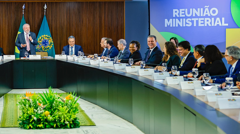 Luiz Inácio Lula da Silva durante reunião ministerial no Palácio do Planalto. Ele está em pé e fala ao microfone. Ao lado, ministros sentados em uma mesa