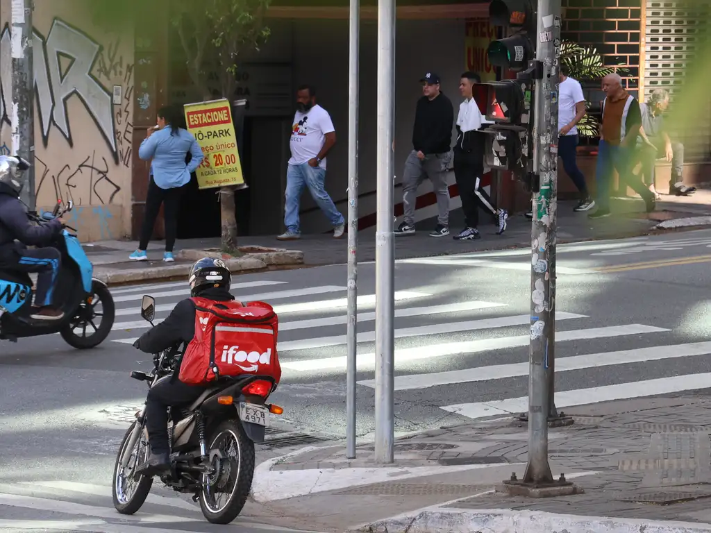 Motociclista entregador da plataforma ifood em São Paulo. Ele está na moto, com roupa preta e mochila vermelha