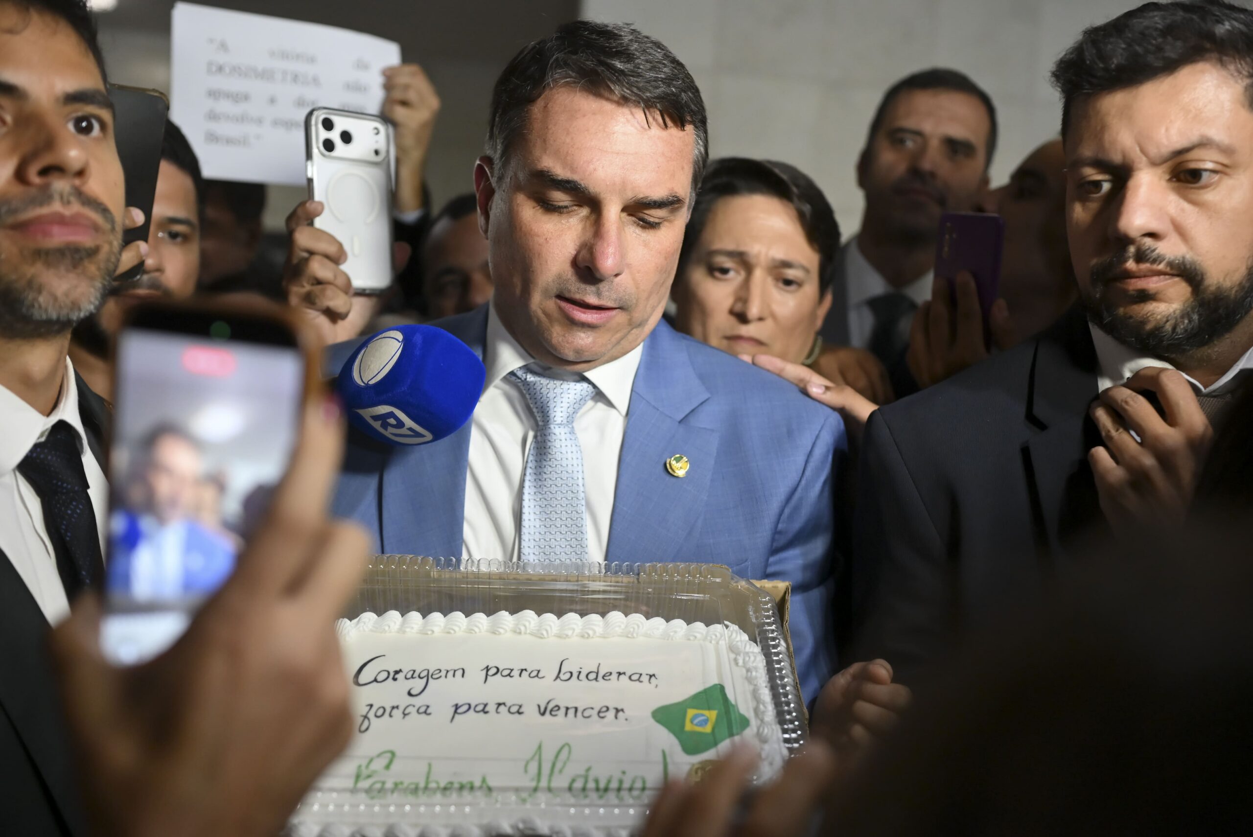 Flávio Bolsonaro, um homem branco, está cercado por pessoas.